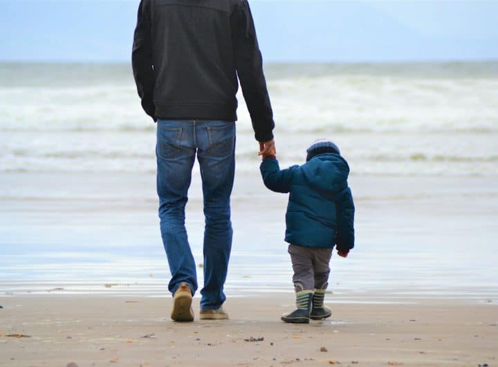 man and boy walking on seashore under blue sky