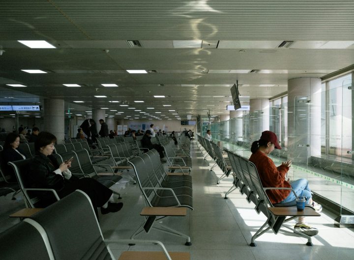 People waiting in a modern airport lounge by large windows.